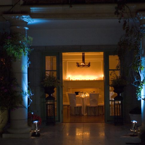 Grand entrance to a luxury private estate illuminated with architectural lighting, candlelit interiors, and elegant landscaping for an evening wedding or special event.
