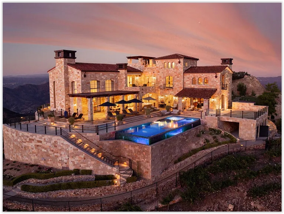 Luxury Malibu vineyard estate at sunset featuring Tuscan-inspired architecture, an infinity pool, rolling vineyards, and panoramic mountain views.