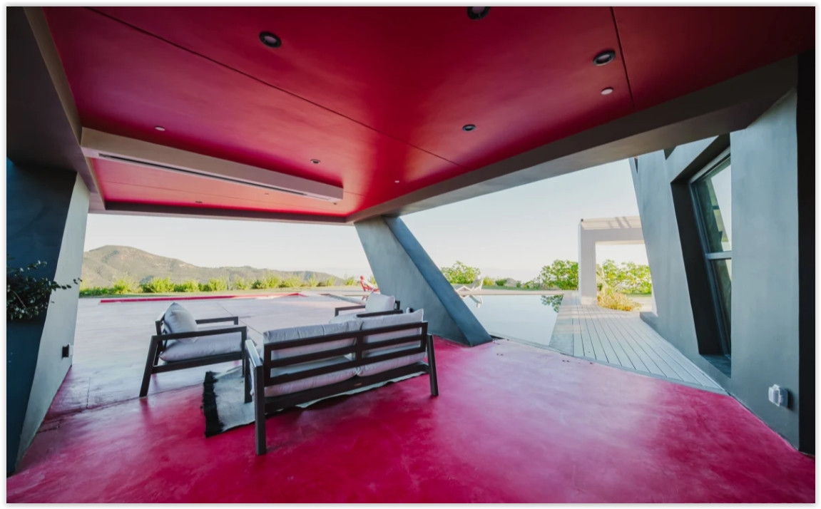 Covered outdoor lounge overlooking the pool and surrounding Malibu hills, designed for seamless indoor-outdoor living.