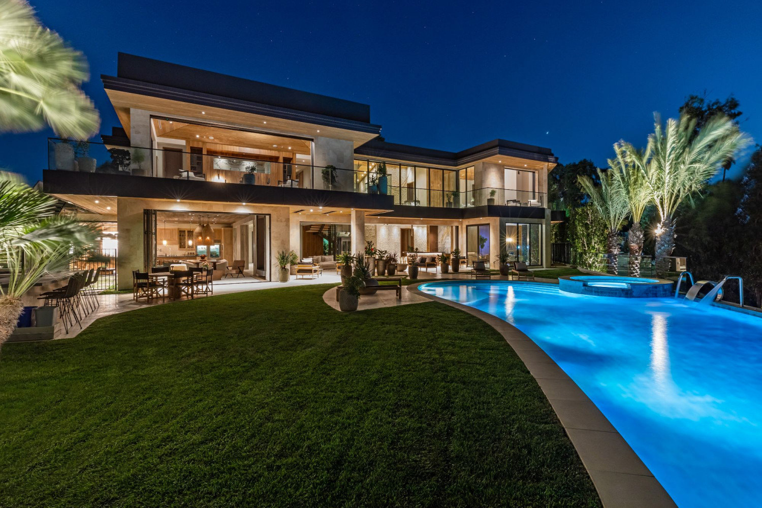 Contemporary Beverly Hills estate illuminated at twilight with a resort-style pool, elegant outdoor entertaining spaces, and striking modern architecture.