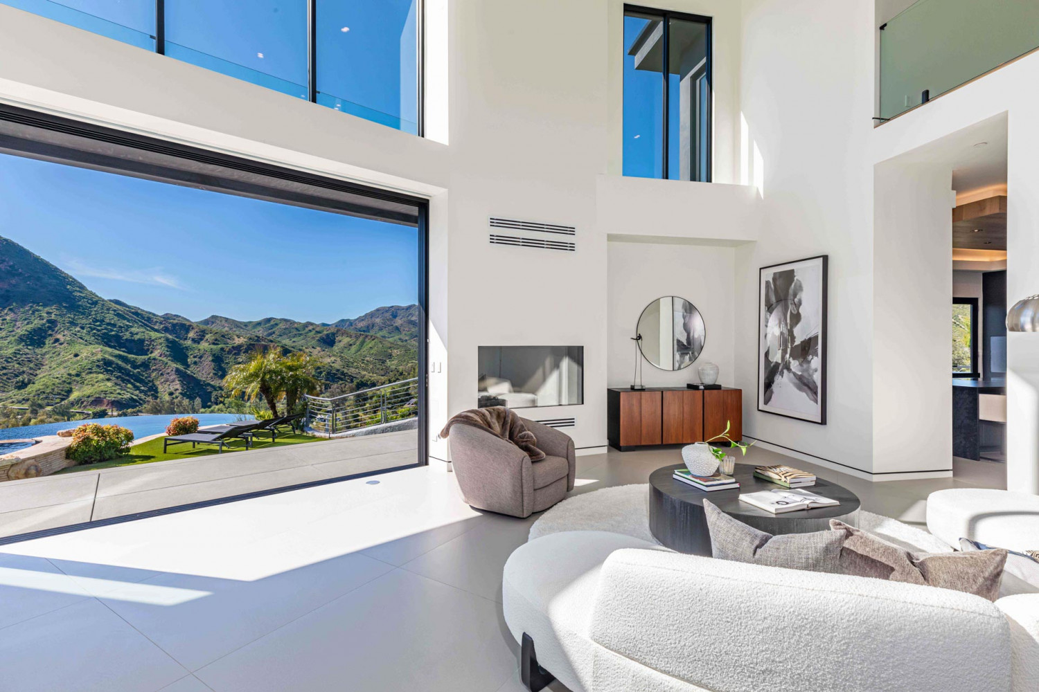 Modern living room with sculptural seating and floor-to-ceiling glass overlooking hillside canyon views in Agoura Hills estate.