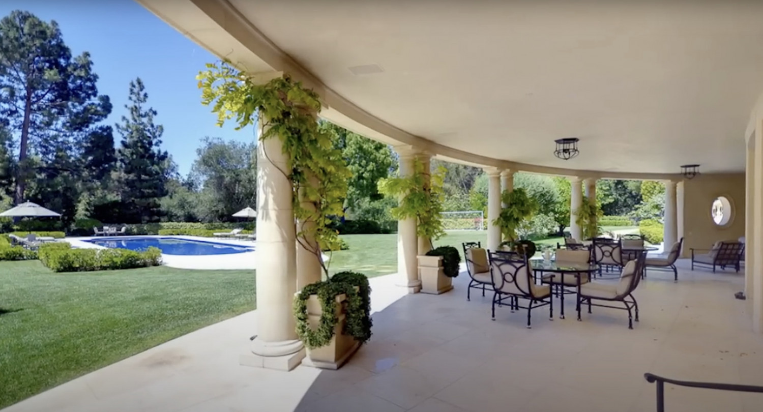 Covered outdoor entertaining terrace overlooking the pool and gardens at a luxury private estate.