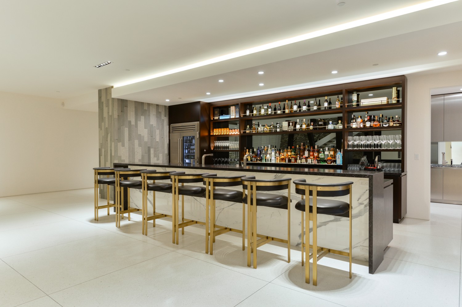 Private bar with marble counters, brass stools and built-in shelving for entertaining