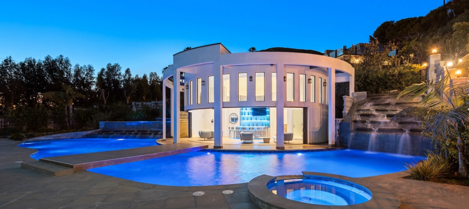 Luxury Malibu ocean view estate with illuminated resort-style pool and iconic circular pavilion at sunset